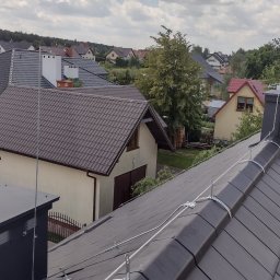 INSTAL-KON MACIEJ KONWA - Antena odgromowa zamontowana na kominie i dachu z dachówki ceramicznej na tle zabudowy jednorodzinnej w słoneczny dzień.