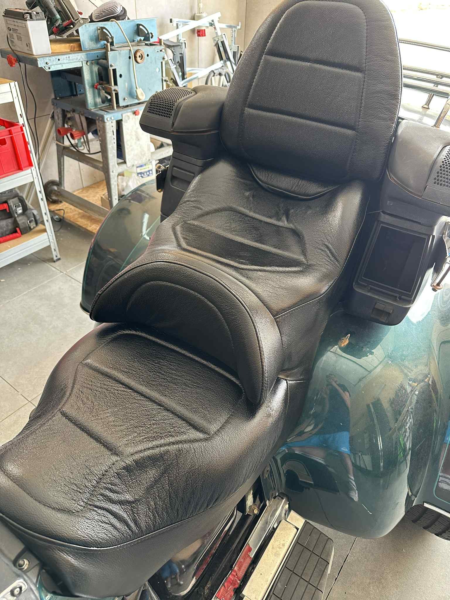 Czarne, skórzane siedzenie motocyklowe z wyraźnymi przeszyciami, widoczne w warsztacie, sugerujące renowację lub naprawę tapicerki.