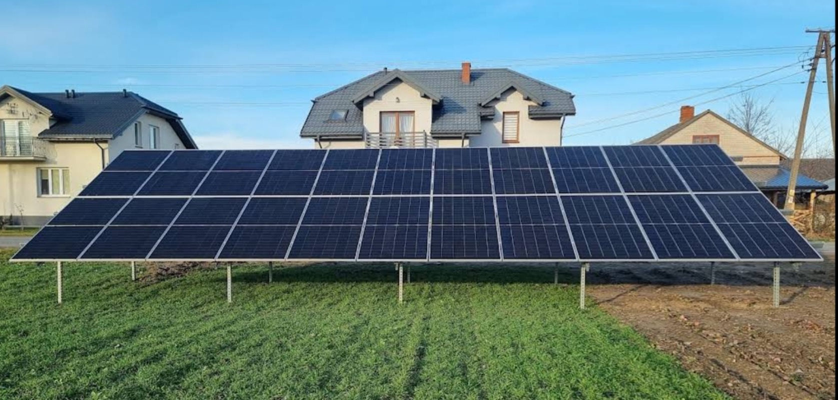 Instalacja paneli słonecznych na metalowej konstrukcji na trawniku przed domami jednorodzinnymi.