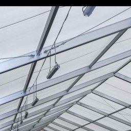 SUNPOWER Sylwester Lemański - Metalowa konstrukcja dachu z zamontowanymi lampami wiszącymi na przewodach, widok z dołu.