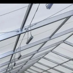 Metalowa konstrukcja dachu z zamontowanymi lampami wiszącymi na przewodach, widok z dołu.