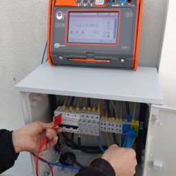 SUNPOWER Sylwester Lemański - Elektryk wykonuje pomiary impedancji pętli zwarcia ZL-PE = 0,356 Ω w rozdzielnicy za pomocą miernika Sonel, widoczne przewody pomiarowe i listwa zaciskowa.