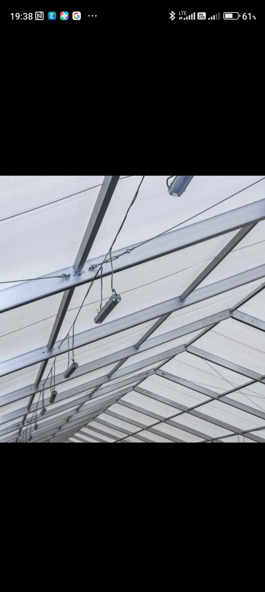 Metalowa konstrukcja dachu z zamontowanymi lampami wiszącymi na przewodach, widok z dołu.