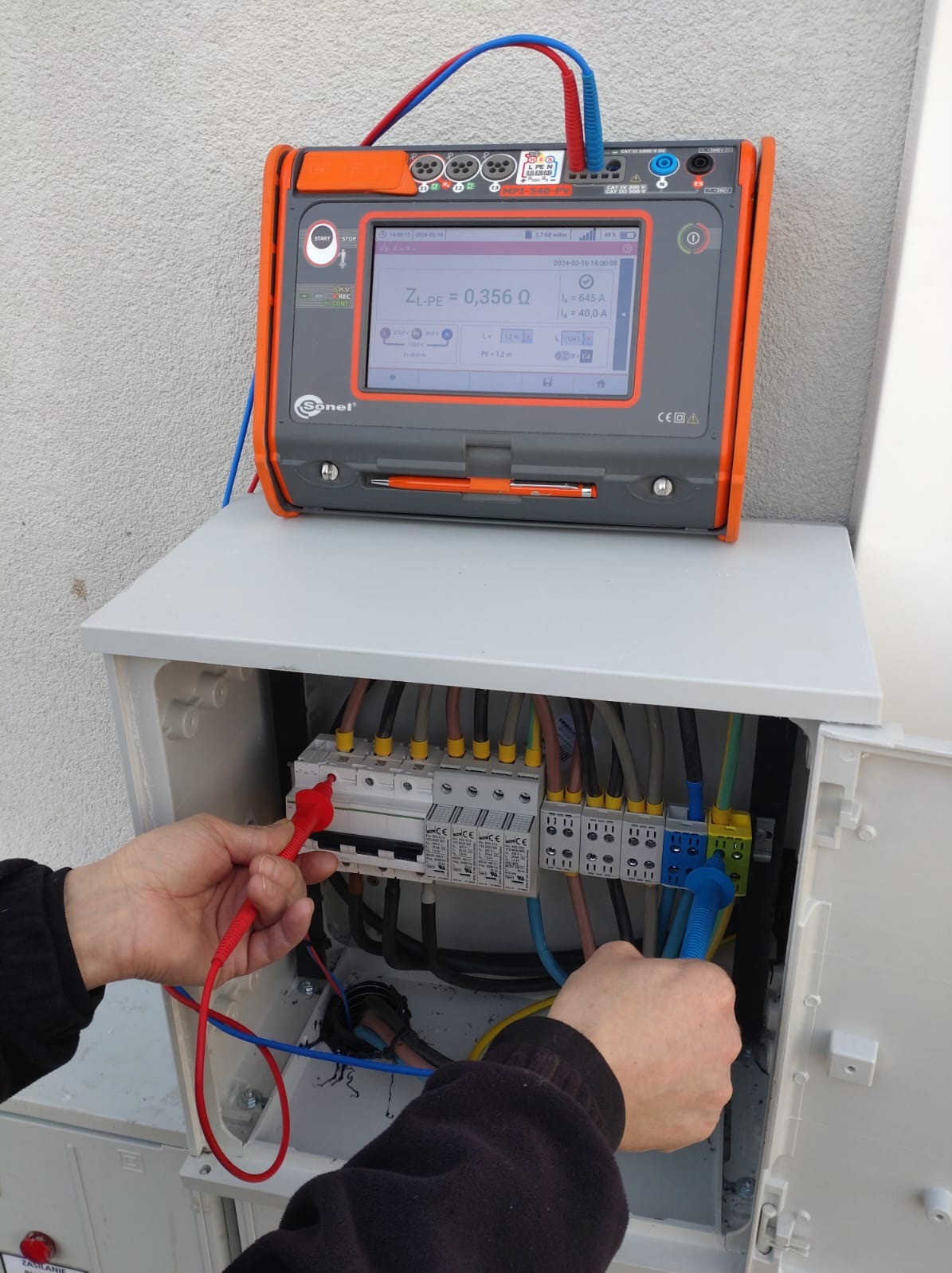 Elektryk wykonuje pomiary impedancji pętli zwarcia ZL-PE = 0,356 Ω w rozdzielnicy za pomocą miernika Sonel, widoczne przewody pomiarowe i listwa zaciskowa.