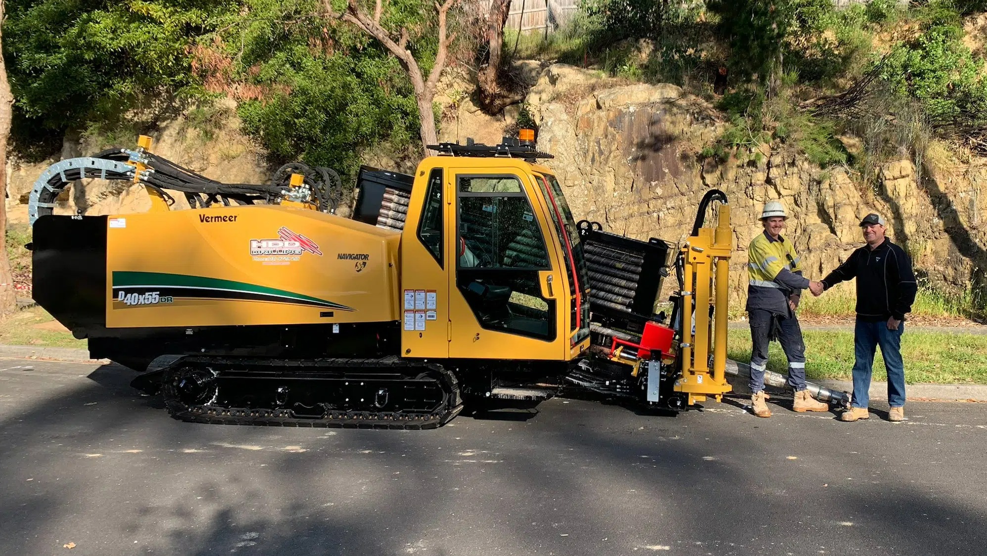Żółta wiertnica kierunkowa Vermeer D40x55DR z dwoma mężczyznami w uścisku dłoni, na tle skalistego wzgórza i zieleni.
