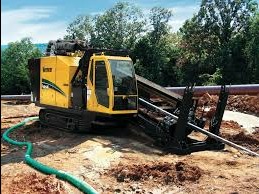 Żółta maszyna do wiercenia horyzontalnego Vermeer na gąsienicach, z widoczną rurą wiertniczą i zielonym wężem, pracująca w ziemi na tle drzew.