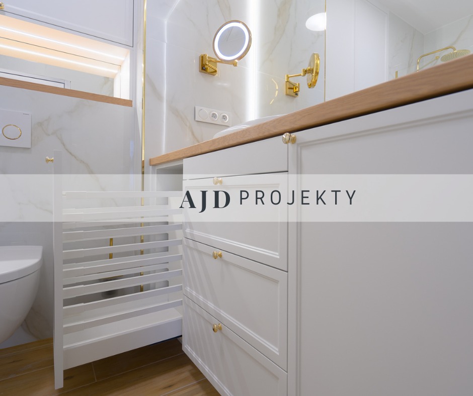 Biała łazienka z marmurowymi ścianami, złotymi akcentami i drewnianym blatem, widoczne szafki z szufladami i wysuwany kosz na pranie.