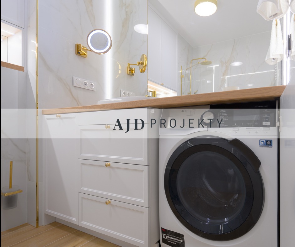 Jasna łazienka z marmurowymi płytkami, złotymi akcentami, białą zabudową meblową z szufladami, drewnianym blatem i pralką AEG z czarnym panelem.