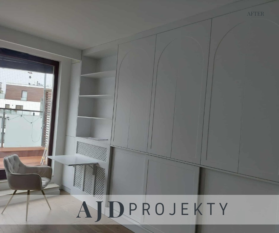 Biała zabudowa meblowa z półkami i szafkami, zintegrowana ze składanym blatem przy oknie balkonowym. Widoczny fotel i napis 'AFTER'.
