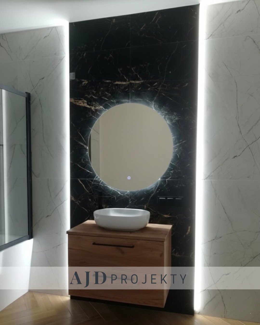 Nowoczesna łazienka z okrągłym lustrem LED, umywalką nablatową na drewnianej szafce i czarnym marmurem na ścianie, oświetlona pionowymi pasami LED.