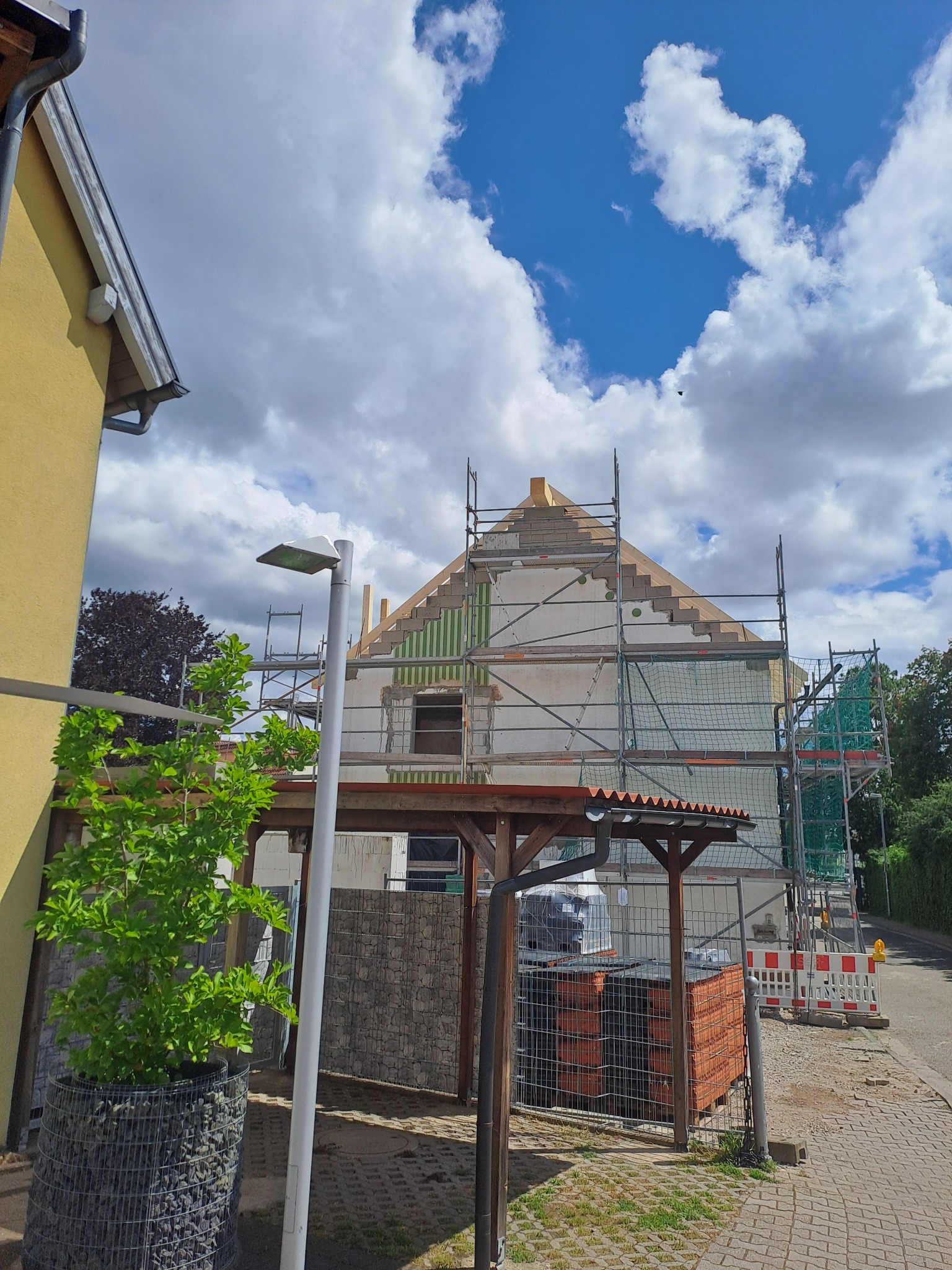 Dom w trakcie remontu, z widocznym rusztowaniem i przygotowywanym nowym poszyciem dachowym, częściowo ocieplony, na tle błękitnego nieba z chmurami.