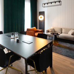 Tuwima 48 Sp. z o.o. - Nowoczesna sala konferencyjna z dużym stołem, krzesłami, sofą i stylowym oświetleniem. Aranżacja wnętrza biura z elementami dekoracyjnymi i roślinami.