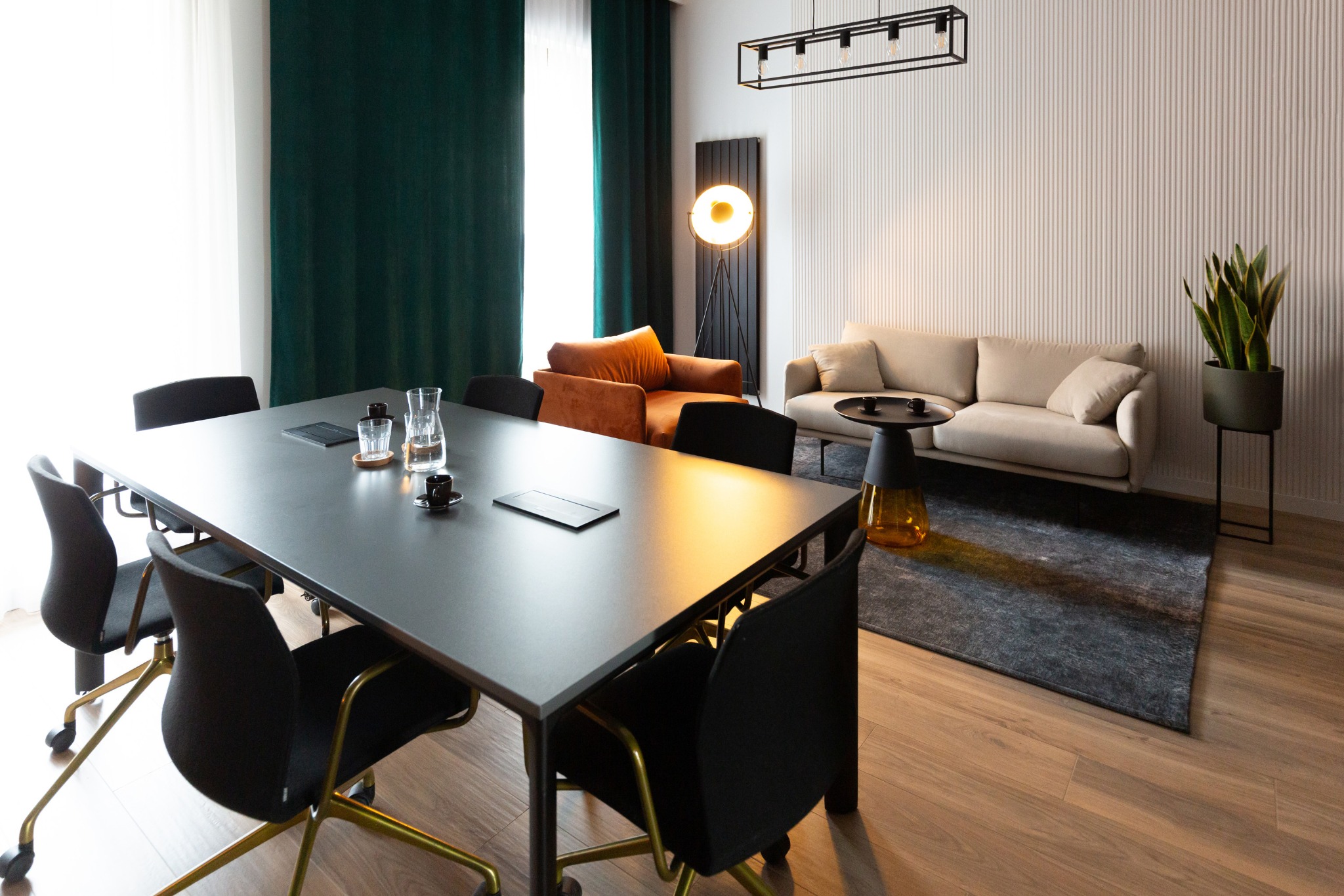 Nowoczesna sala konferencyjna z dużym stołem, krzesłami, sofą i stylowym oświetleniem. Aranżacja wnętrza biura z elementami dekoracyjnymi i roślinami.