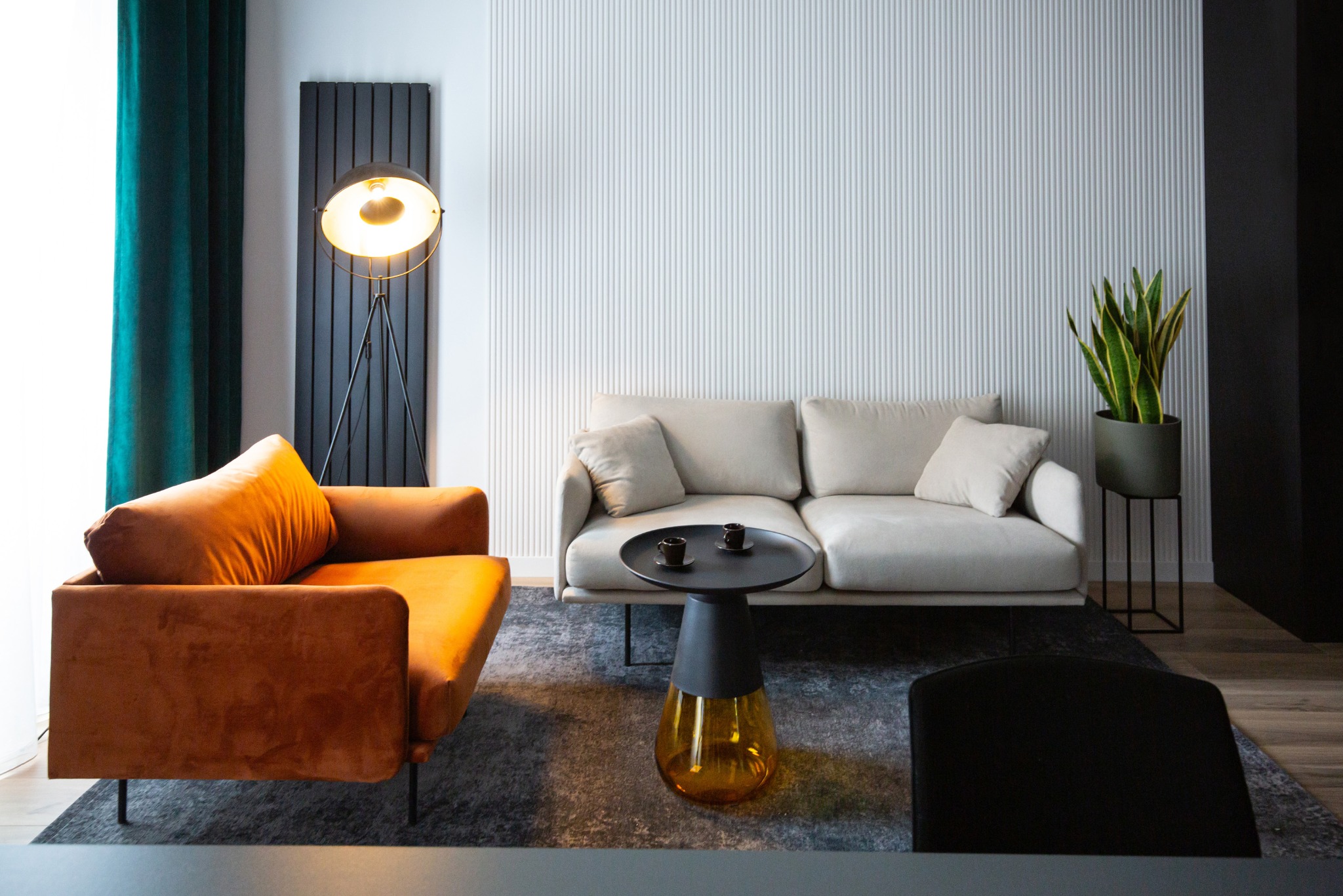 Stylowe wnętrze biura z sofą, fotelem i lampą stojącą. Minimalistyczny design, nowoczesne meble, roślina doniczkowa. Przytulna aranżacja przestrzeni biurowej.