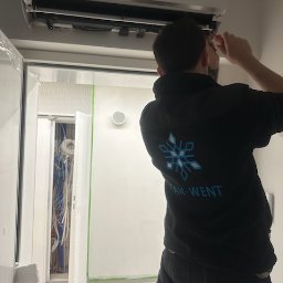 Star-Went PATRYK DULĘBA - Instalator w bluzie z logo STAR-WENT montuje klimatyzację w pomieszczeniu z widocznymi kablami i otwartymi drzwiami.
