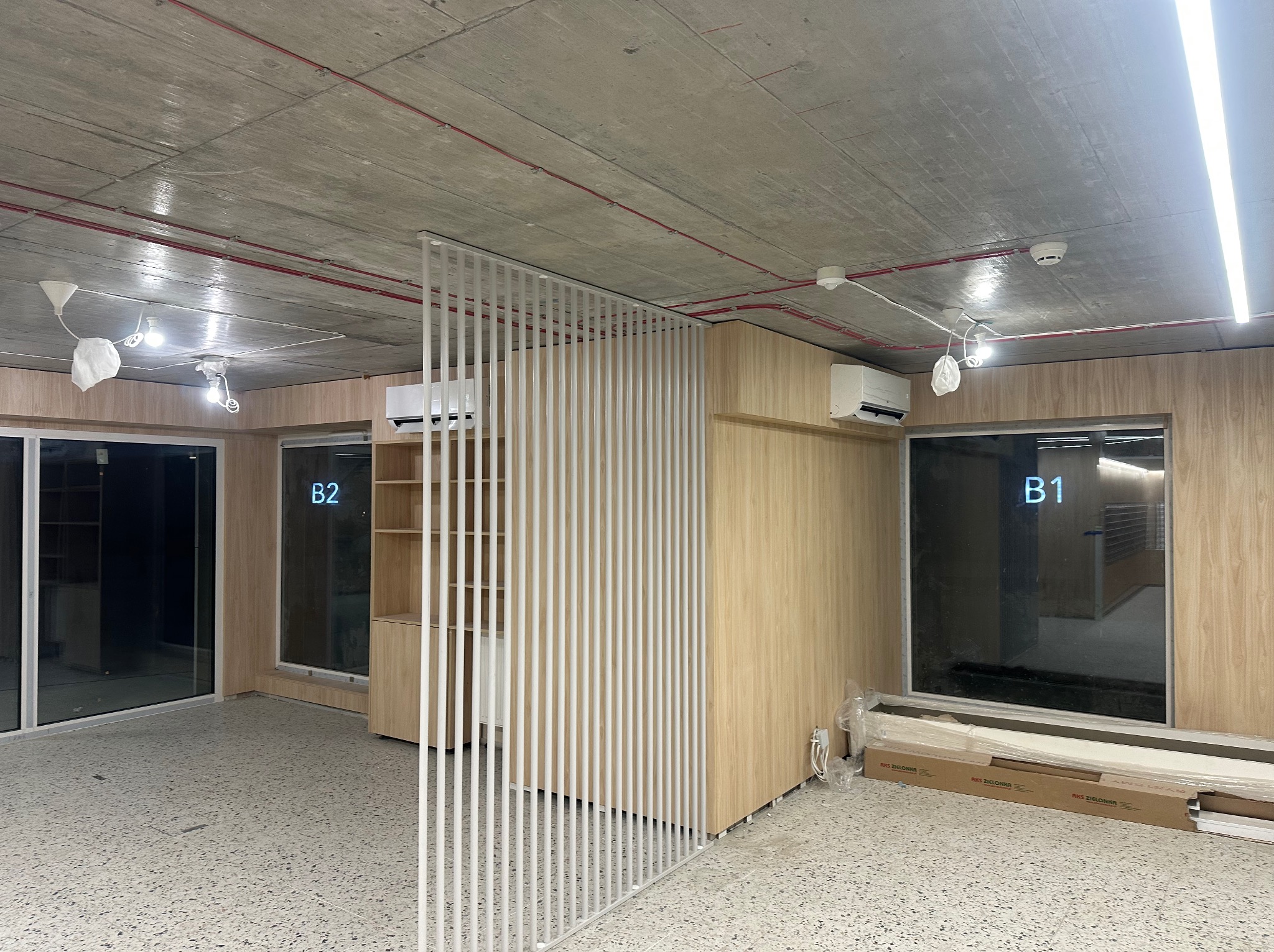 Wnętrze biurowe w stanie deweloperskim z zamontowaną klimatyzacją split na ścianie, widoczne elementy instalacji wentylacyjnej pod sufitem, oraz materiały budowlane czekające na montaż.