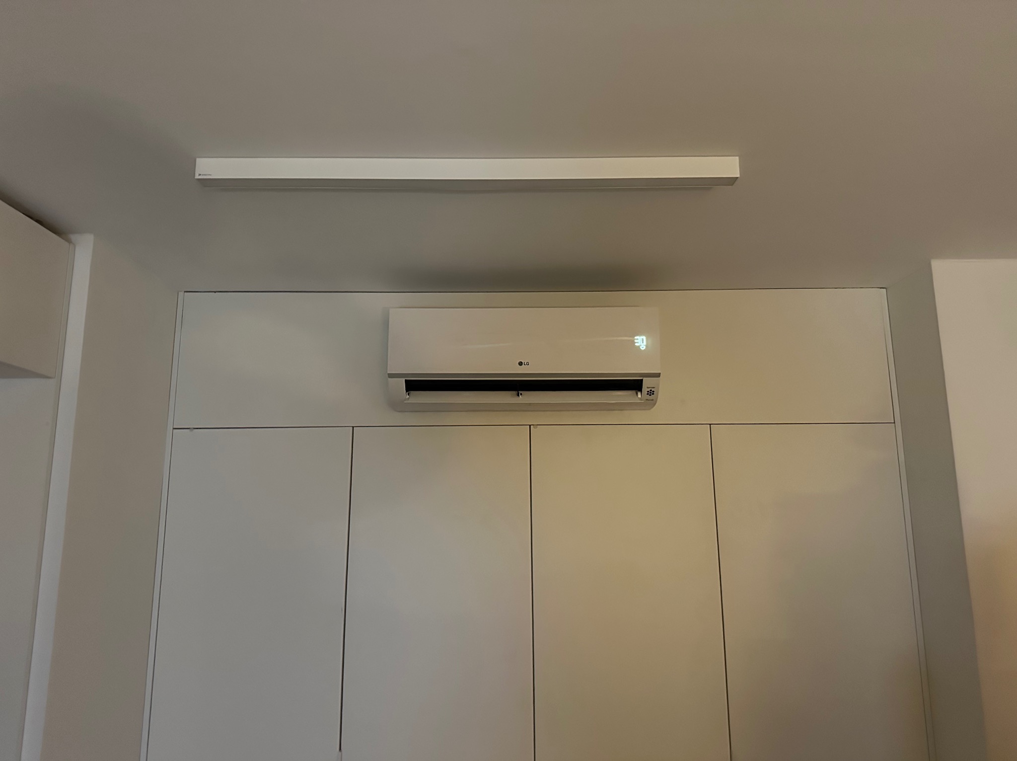 Biała klimatyzacja LG zamontowana nad szafkami w minimalistycznym wnętrzu, widoczny wyświetlacz temperatury 30 stopni.