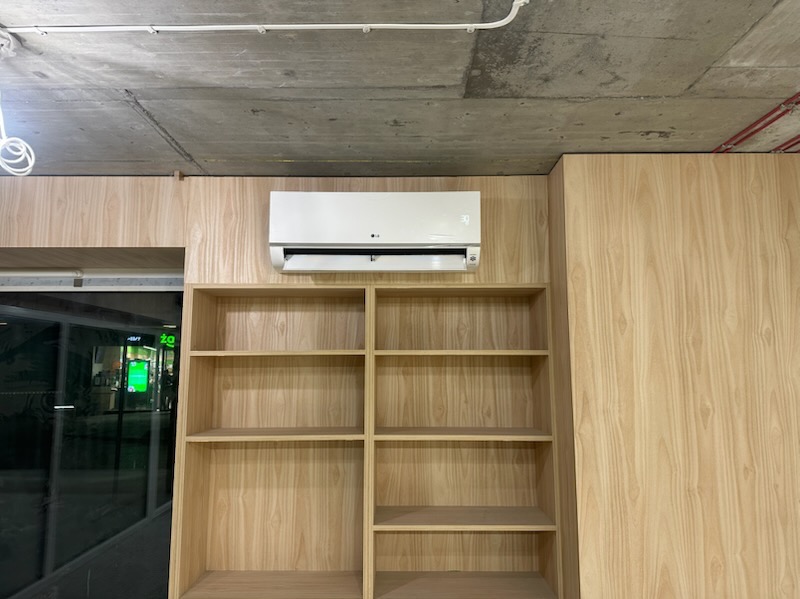 Biała jednostka klimatyzacyjna LG zamontowana nad pustymi, drewnianymi półkami w biurze w Kielcach, widok z dołu na betonowy sufit z instalacjami.