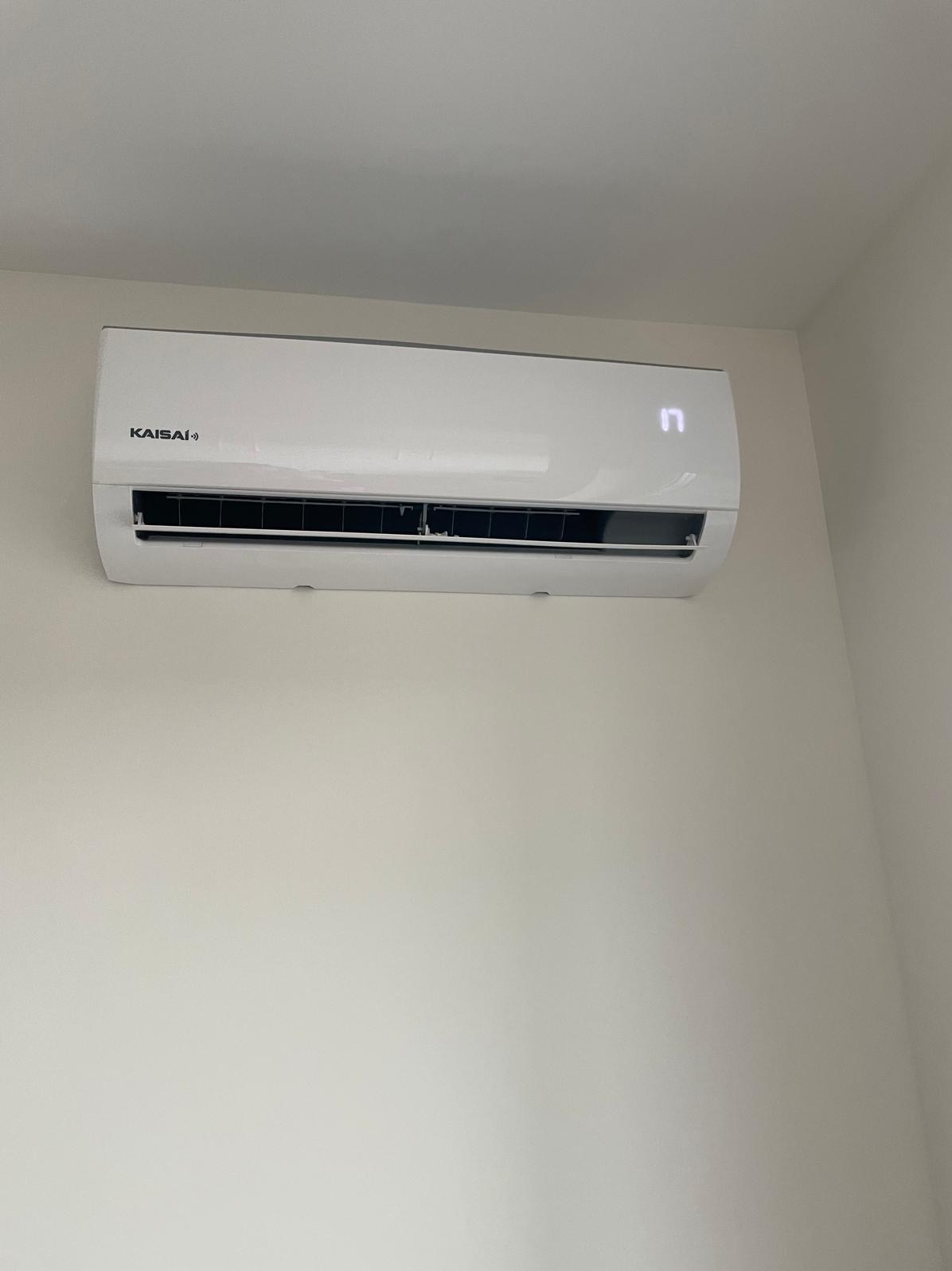 Biały klimatyzator Kaisai zamontowany na jasnej ścianie, widoczny wyświetlacz z cyfrą 17.