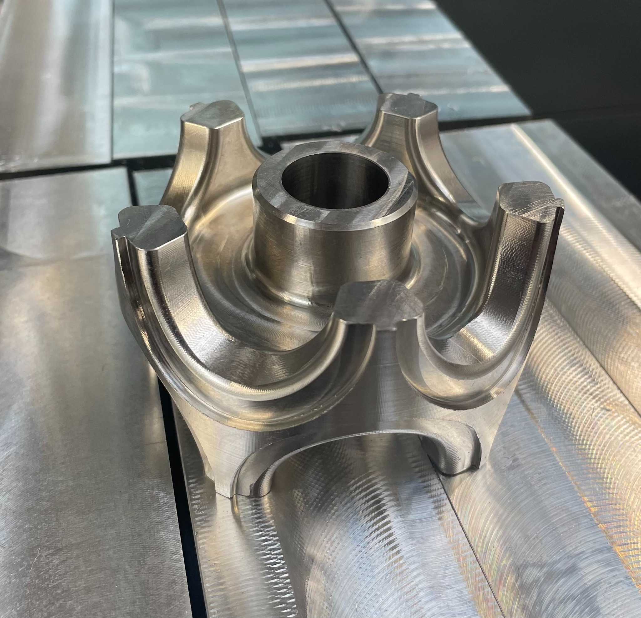 Metalowy element po obróbce skrawaniem, widoczne ślady frezowania na powierzchni, precyzyjnie wykonane detale, cztery ramiona z wgłębieniami, centralny otwór.