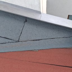 Adex - Szczegółowe ujęcie fragmentu dachu z papy termozgrzewalnej i skorodowanej rynny w Warszawie. Widoczne połączenia papy i metalowe elementy.