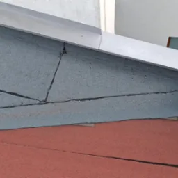 Szczegółowe ujęcie fragmentu dachu z papy termozgrzewalnej i skorodowanej rynny w Warszawie. Widoczne połączenia papy i metalowe elementy.