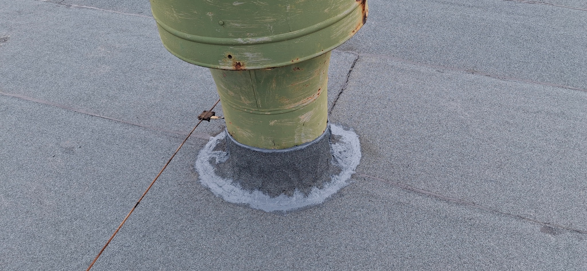 Wykończenie komina na dachu pokrytym papą. Zielony komin zabezpieczony szarą masą uszczelniającą. Widoczne ślady rdzy na kominie.