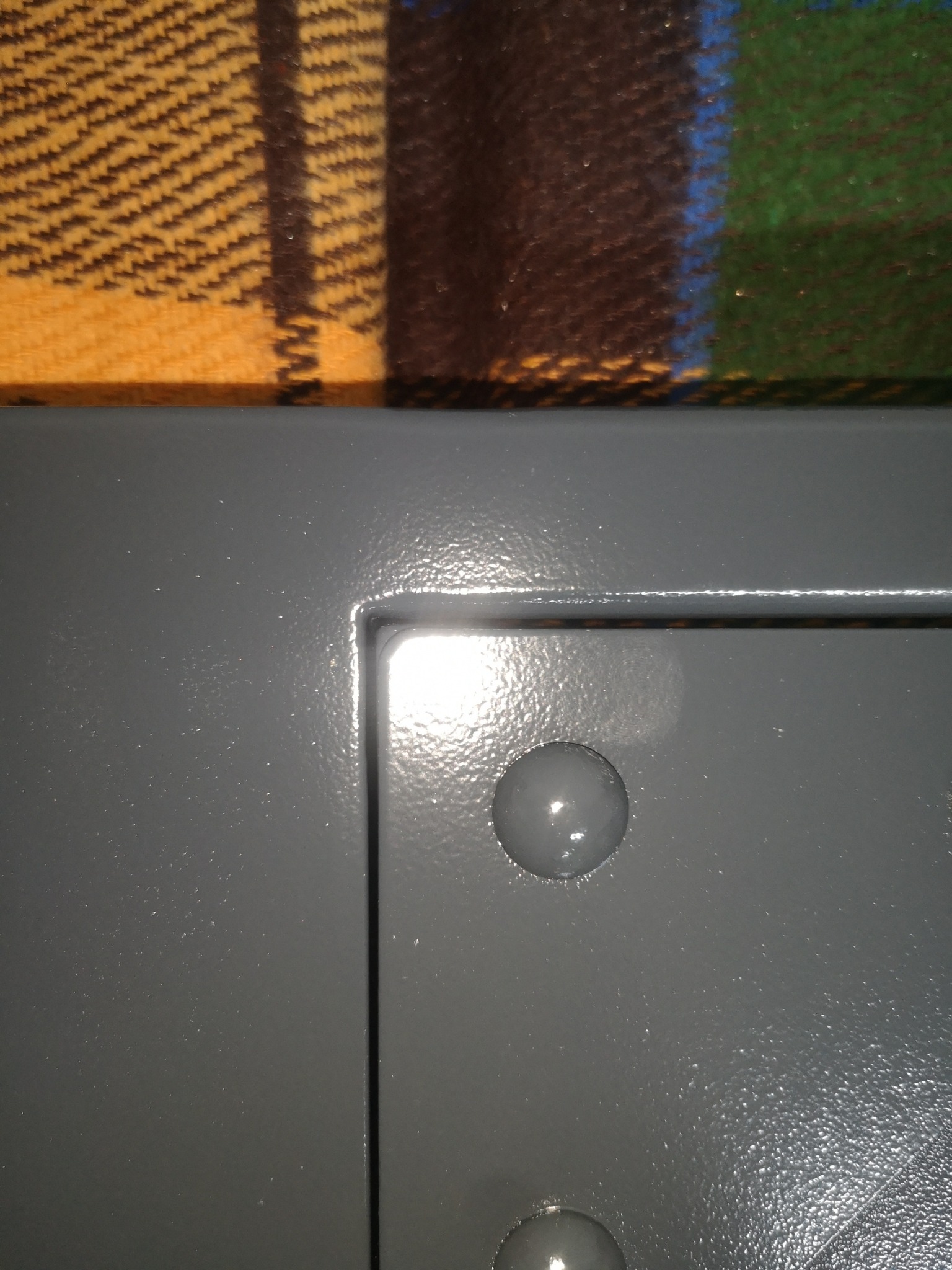 Szczegół szarej, metalowej konstrukcji ze śrubami z zaokrąglonymi łbami na tle wzorzystego koca.