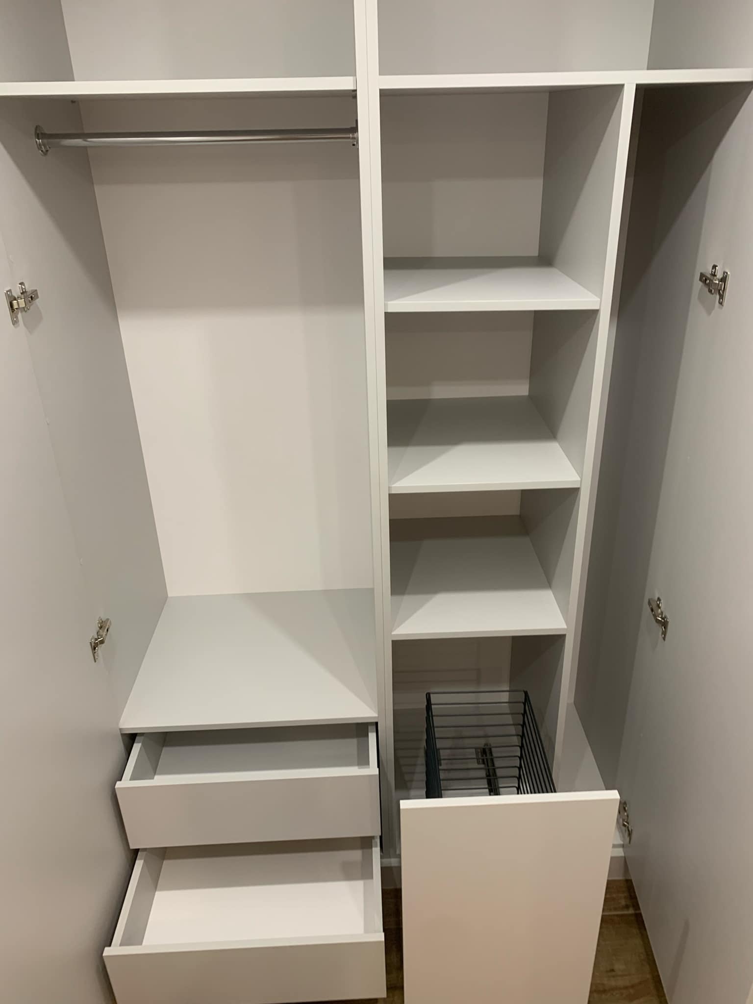 Wnętrze białej szafy z otwartymi drzwiami, widoczne półki, szuflady i metalowy drążek na ubrania.