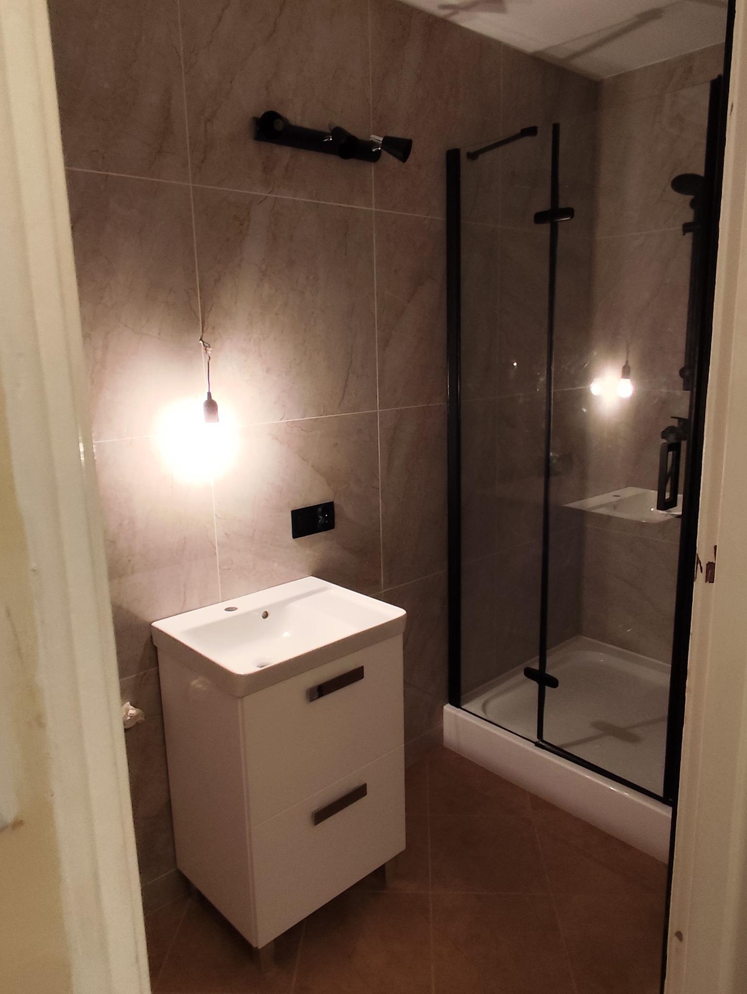 Ukończona aranżacja łazienki w Pruszczu Gdańskim z kabiną prysznicową z czarnymi profilami, białą szafką pod umywalką i płytkami imitującymi kamień na ścianach.