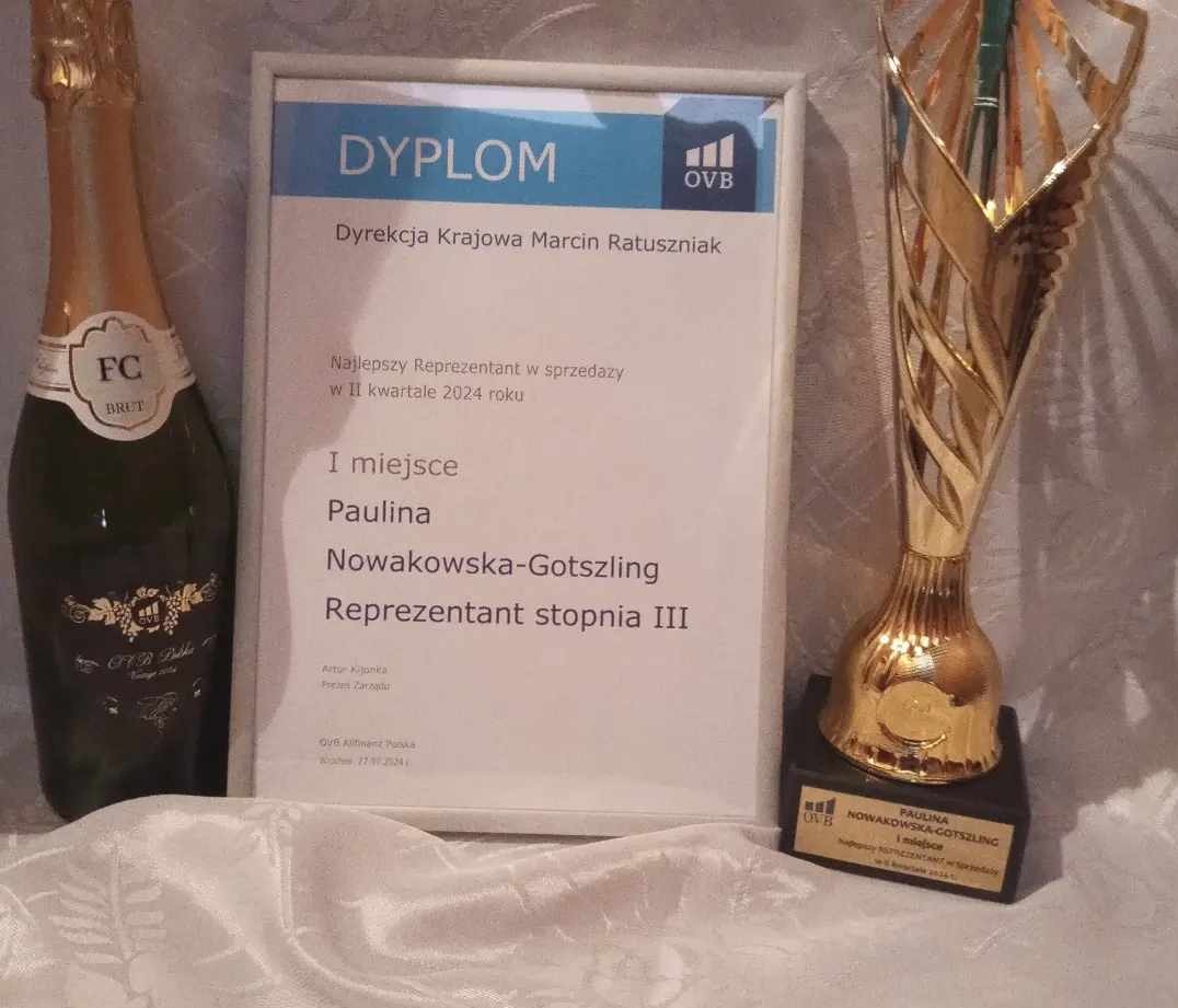 Butelka szampana, dyplom dla najlepszego reprezentanta w sprzedaży w II kwartale 2024 oraz złota statuetka na białym obrusie, gratulacje dla Pauliny Nowakowskiej-Gotszling.