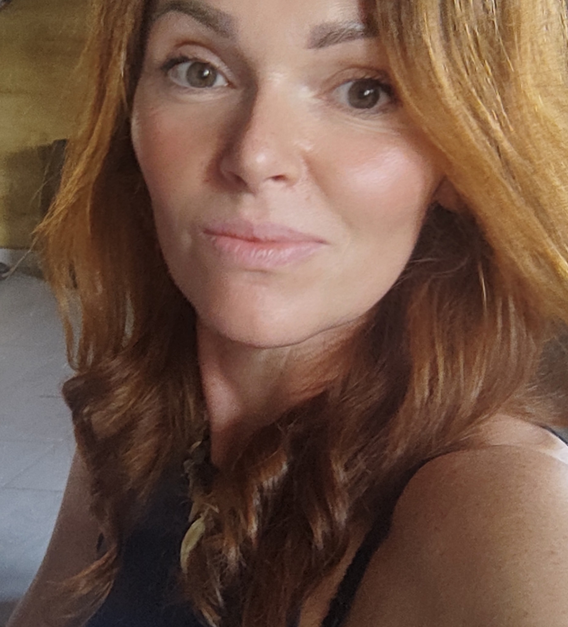 Portret kobiety z rudymi, kręconymi włosami i delikatnym makijażem, noszącej naszyjnik z zawieszką w kształcie liścia.