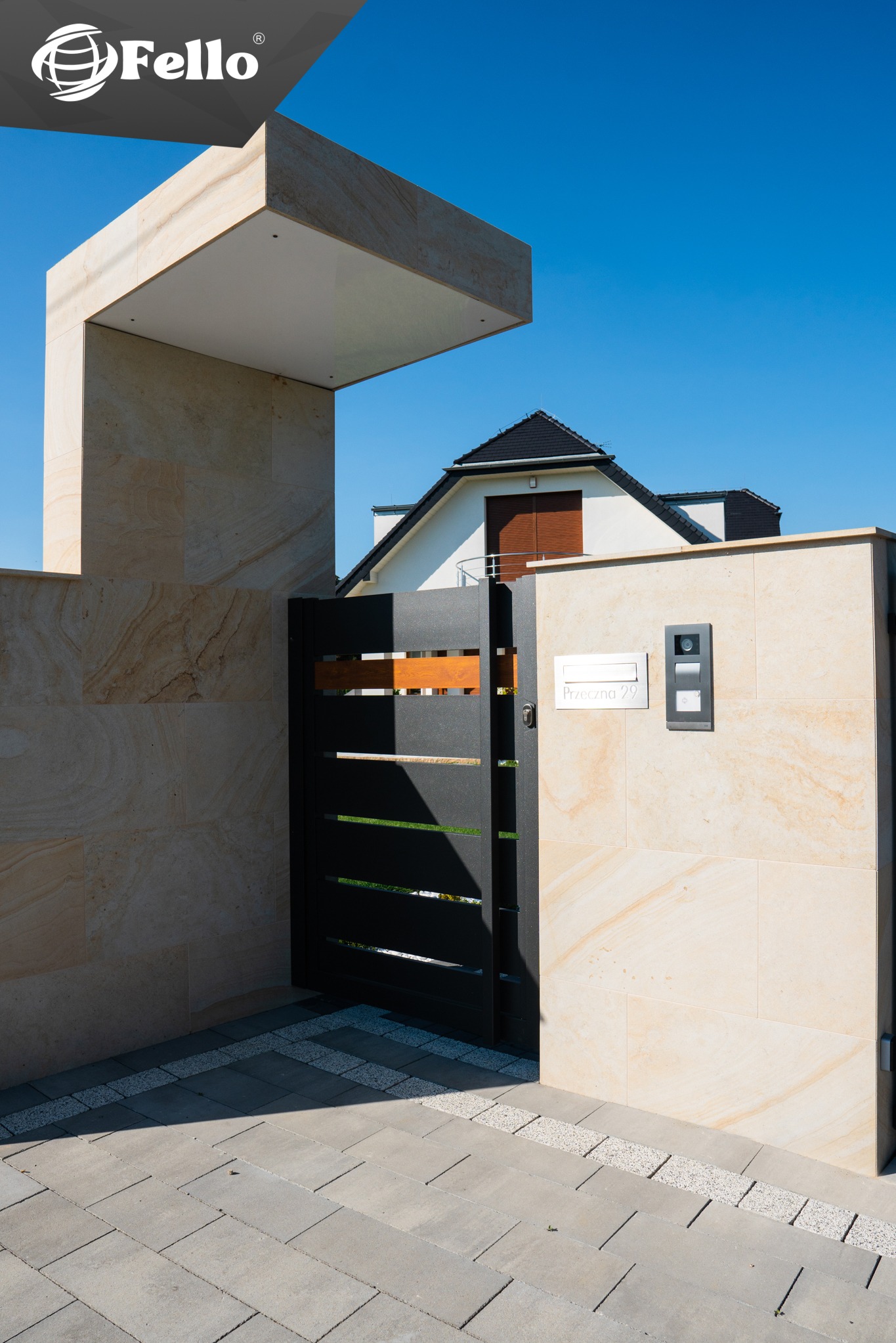 Nowoczesna brama wjazdowa z czarnymi, poziomymi panelami i elementami drewna, wkomponowana w jasny, kamienny mur z numerem domu i domofonem. Model SOLID.