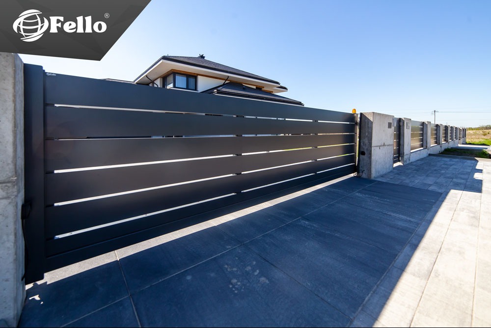 Nowoczesna, przesuwna brama wjazdowa z poziomymi panelami w kolorze antracytowym, zamontowana na betonowych słupkach. Widoczny fragment domu w tle.