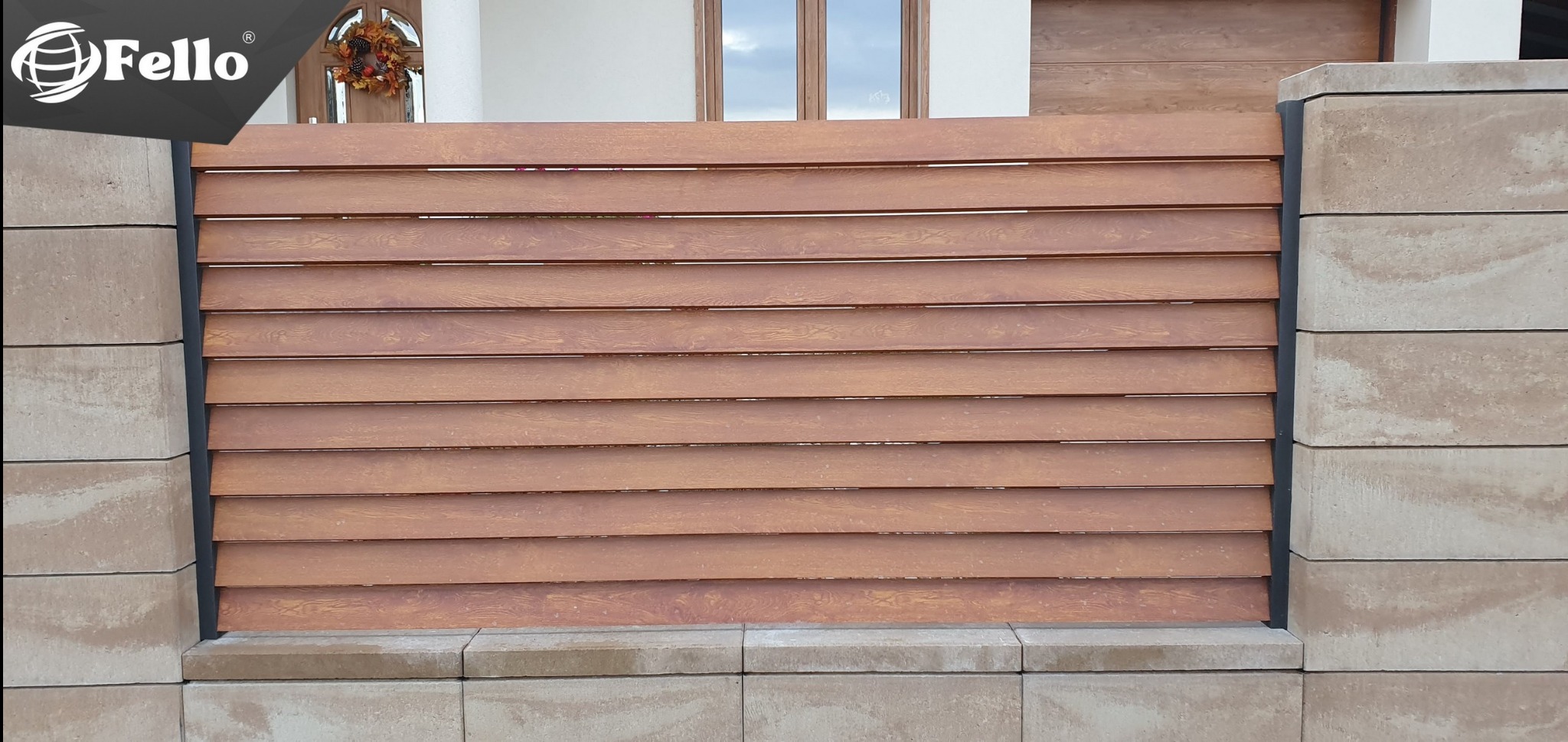 Panelowe ogrodzenie poziome o drewnopodobnej fakturze, osadzone między słupkami z jasnego kamienia. Widoczny fragment domu z drzwiami i oknem.