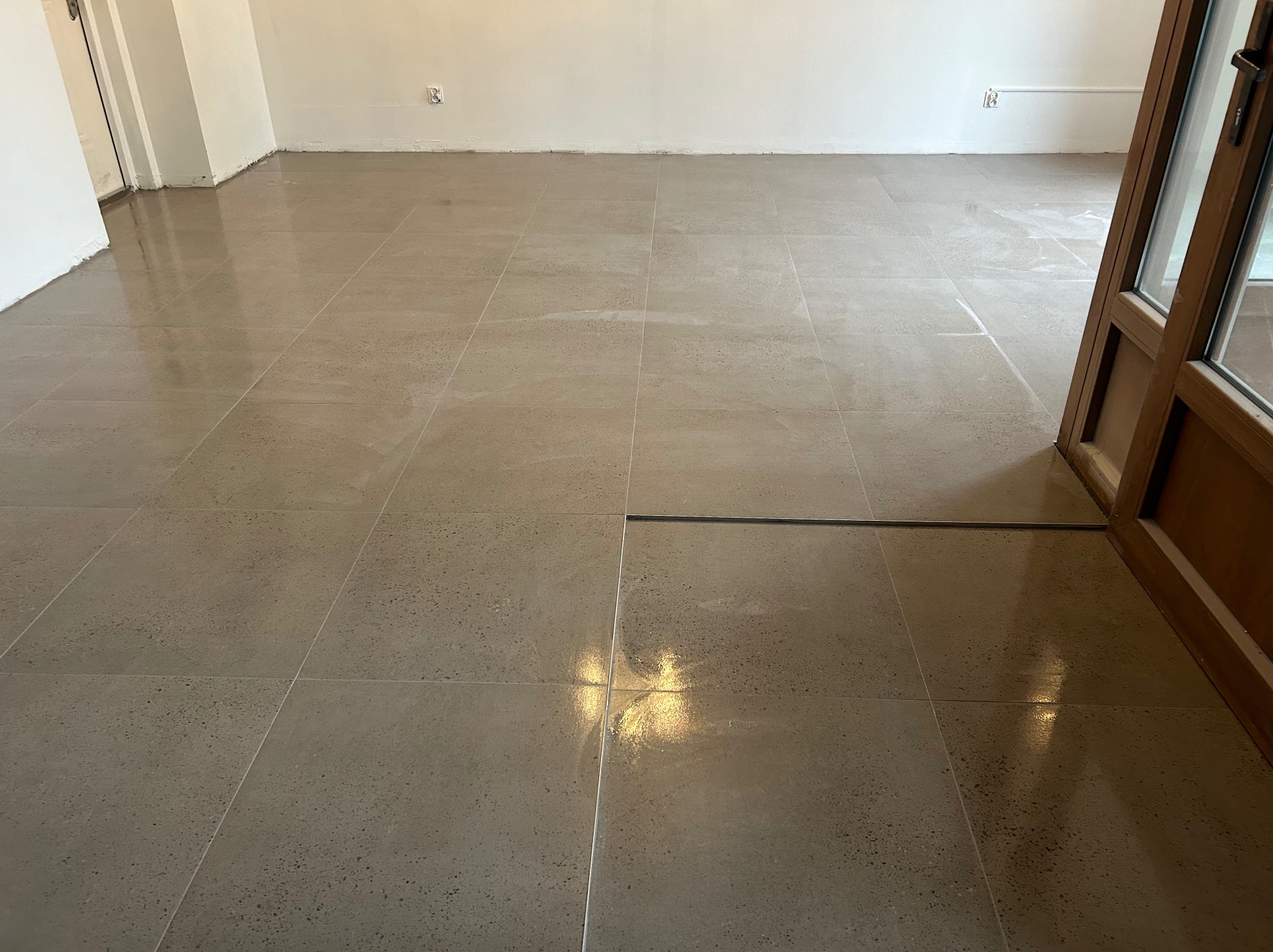 Wykończona podłoga z szarych, kwadratowych płytek w Jaworznie, z widocznym odpływem liniowym i fragmentem drewnianej ościeżnicy drzwiowej.