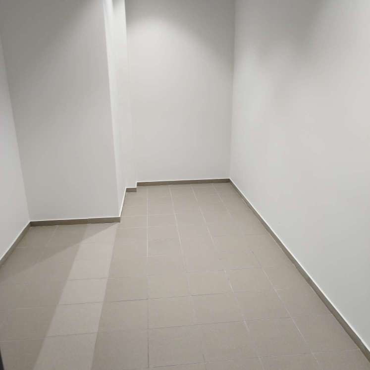 Puste pomieszczenie z szarymi płytkami podłogowymi i białymi ścianami, widok z rogu pokoju.