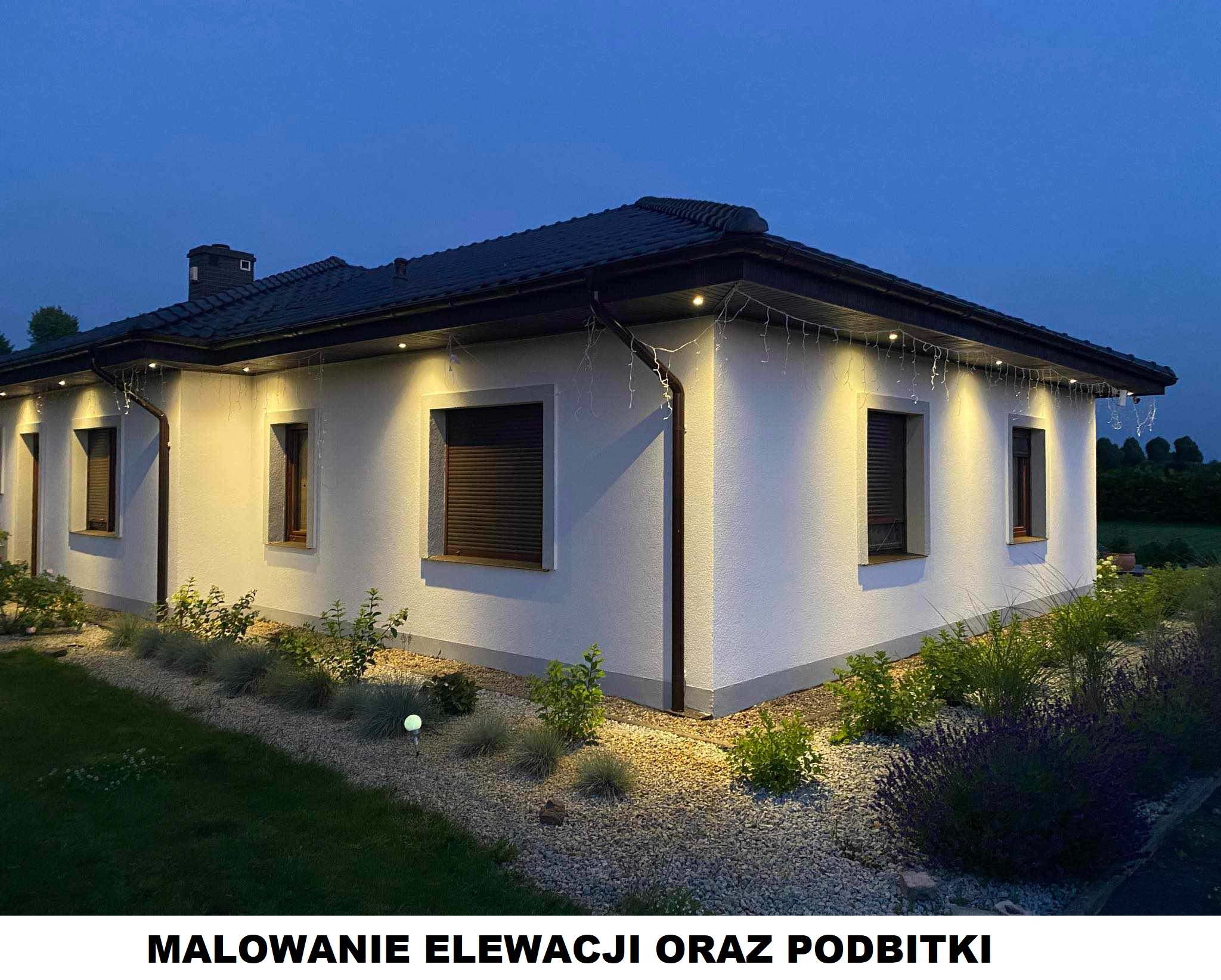 Oświetlona elewacja domu jednorodzinnego z ciemnymi oknami i dachem w wieczornym oświetleniu, widoczne podbitki i oświetlenie ogrodowe.