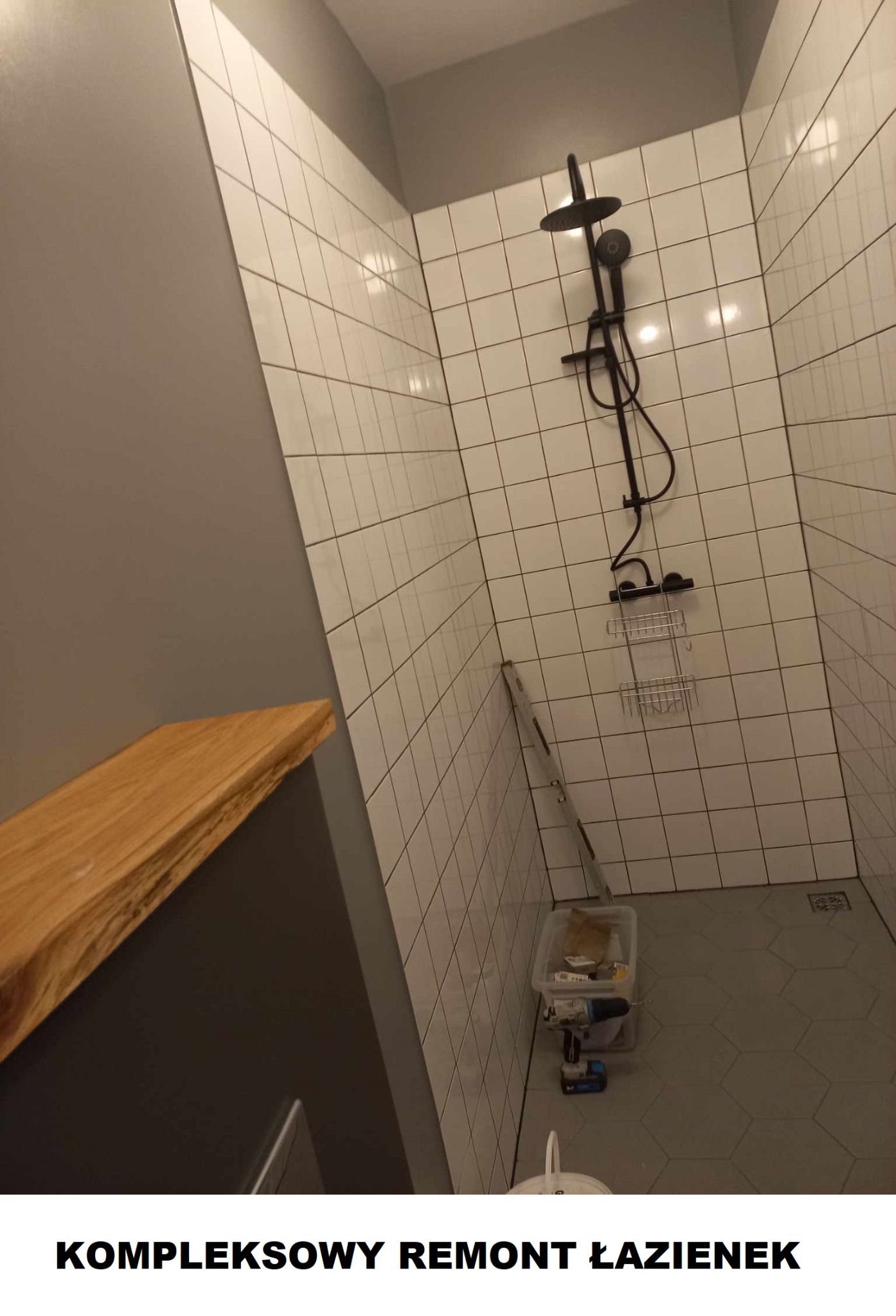 Nowoczesna łazienka z białymi kwadratowymi płytkami na ścianach i heksagonalnymi szarymi płytkami na podłodze, czarna armatura prysznicowa, drewniany blat, drabina oparta o ścianę i pojemnik...