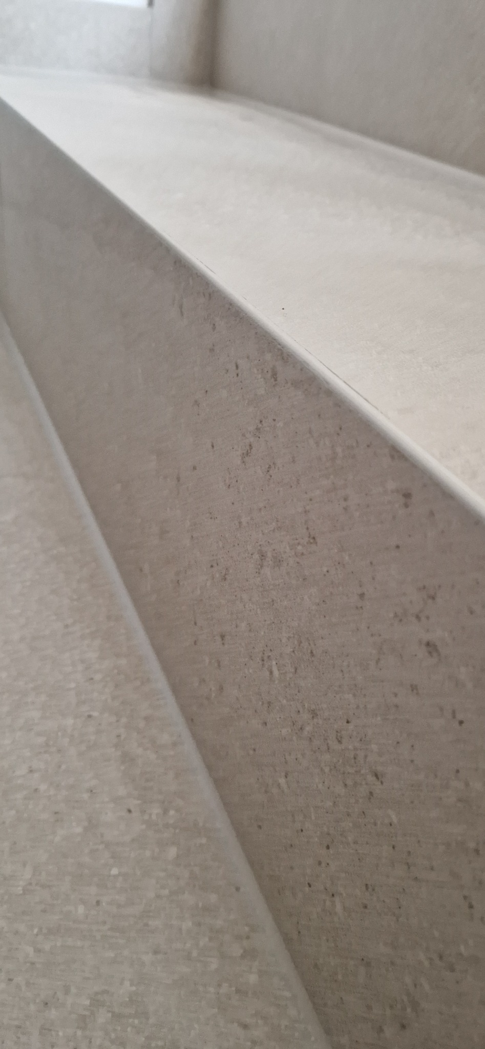 Detaliczne ujęcie kremowych, matowych płytek ceramicznych na schodach, ukazujące ich fakturę i delikatne cieniowanie. Minimalistyczny design wykończenia.