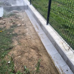 Jackobbruk - Montaż podmurówki z bloczków betonowych pod ogrodzenie panelowe, widoczny pracownik tnący bloczki na wymiar w obłoku pyłu.