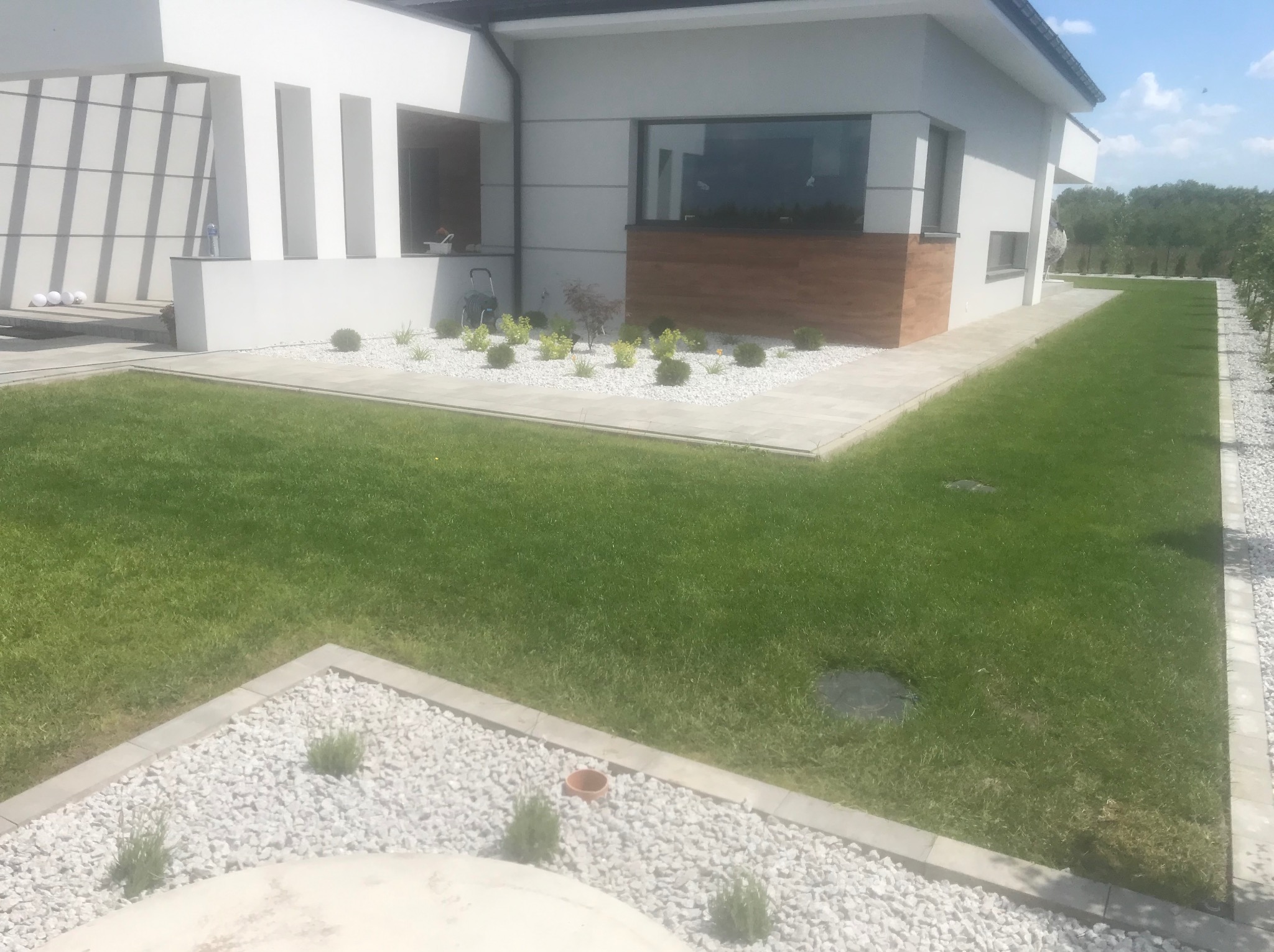 Nowoczesny ogród z białymi kamieniami i zielonym trawnikiem otaczający budynek z dużymi oknami. Estetyczne zagospodarowanie przestrzeni.