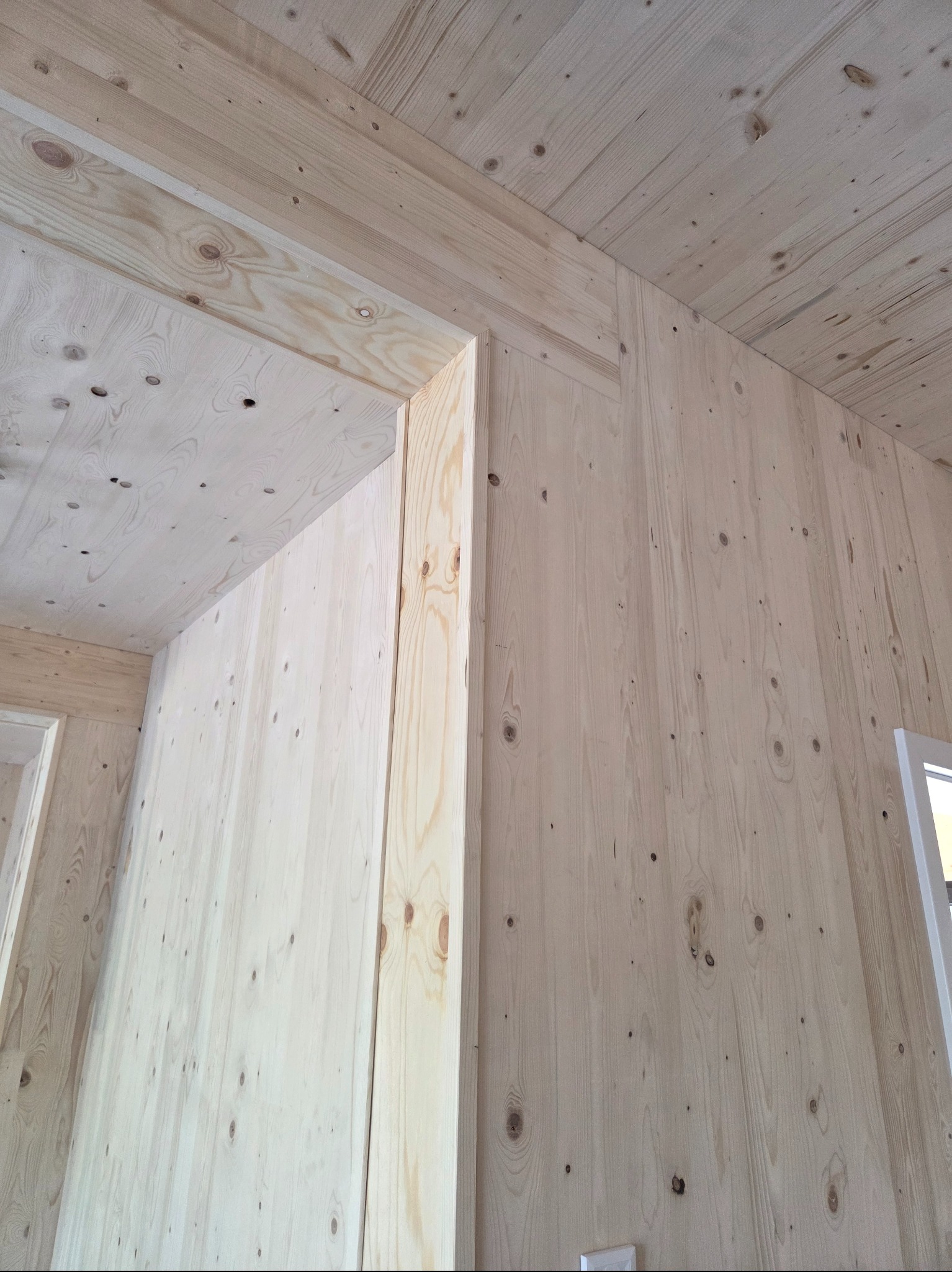 Jasne, drewniane panele ścienne i sufitowe w trakcie montażu. Widoczne łączenia i struktura drewna, surowy stan wykończenia wnętrza.