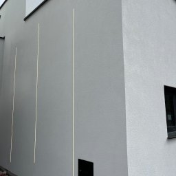 Renova Tomasz Januchowski - Elewacja budynku po nałożeniu białej strukturalnej powłoki z trzema pionowymi, wbudowanymi liniami świetlnymi.
