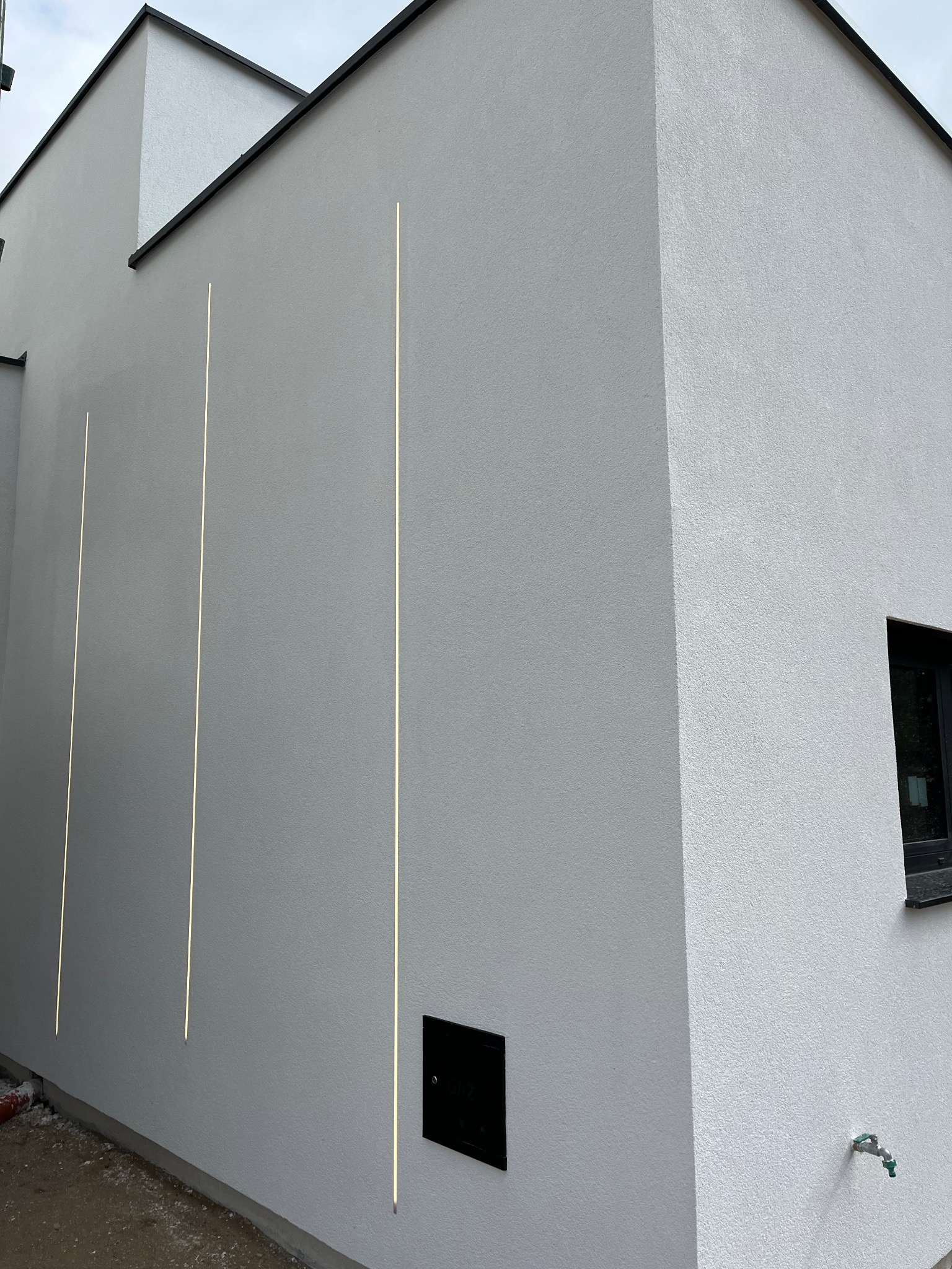 Elewacja budynku po nałożeniu białej strukturalnej powłoki z trzema pionowymi, wbudowanymi liniami świetlnymi.