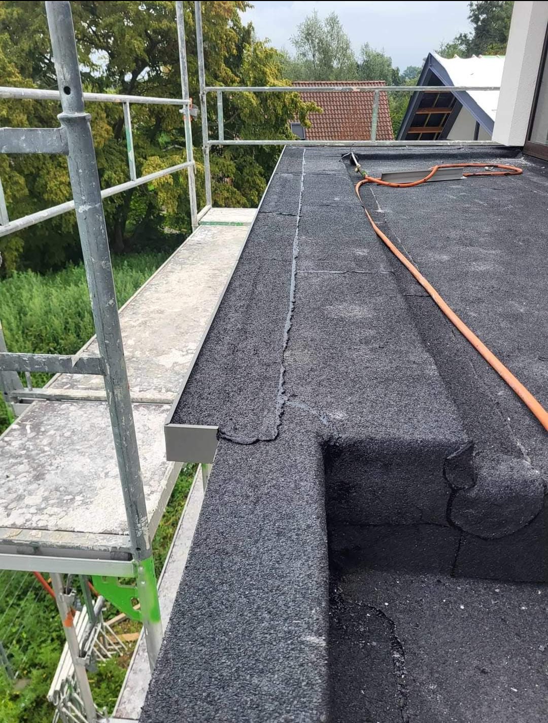 Płaski dach pokryty papą termozgrzewalną, widoczne łączenia i obróbki blacharskie, rusztowanie w tle.