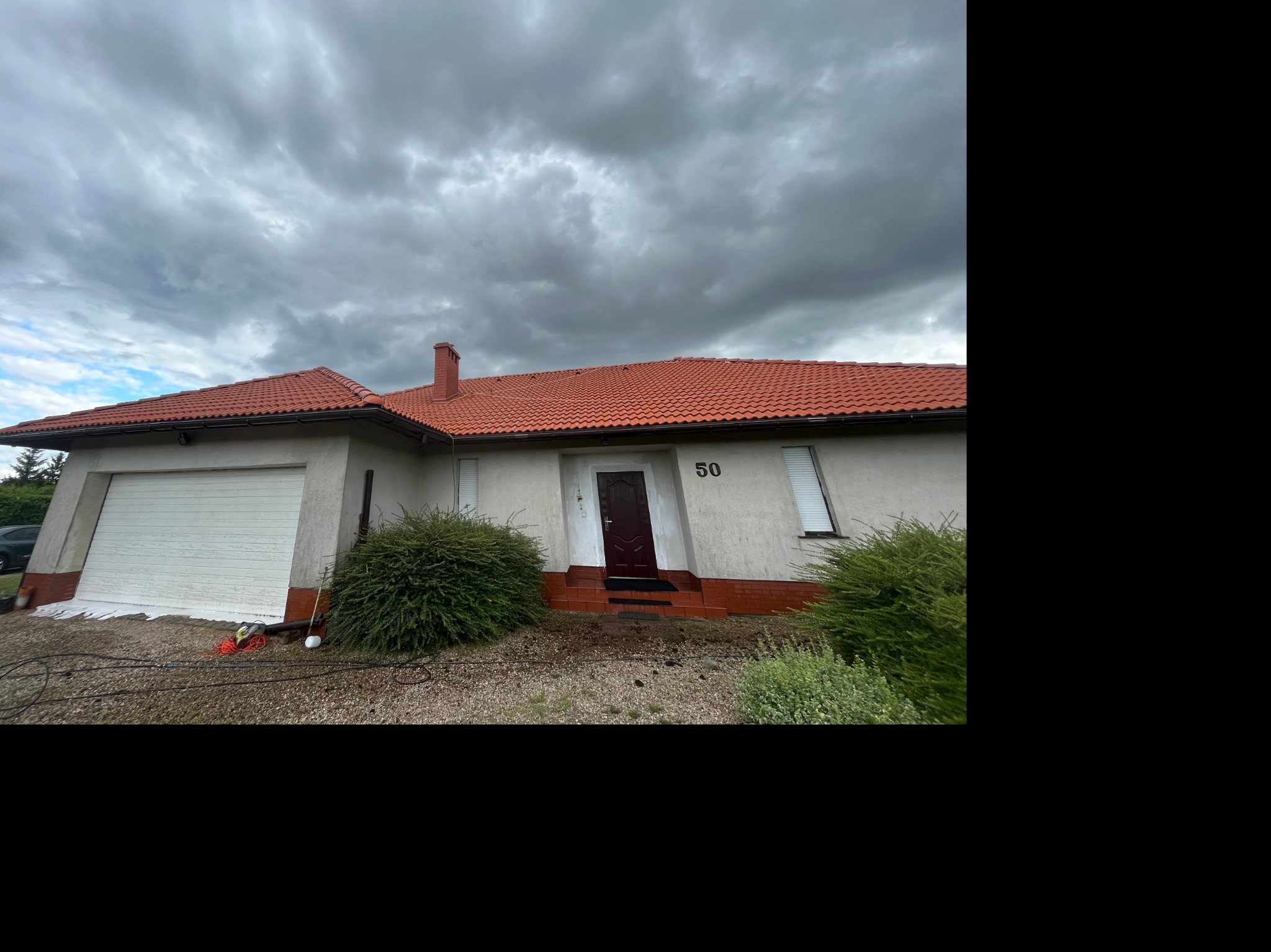 Dom z czerwoną dachówką, elewacją w trakcie mycia, widoczne ślady piany i urządzenia do mycia pod bramą garażową.