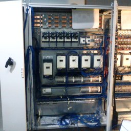 Usługi Elektryczne - Otwarta szafa elektryczna z widocznymi elementami instalacji, w tym licznymi przewodami, stycznikami i zabezpieczeniami, z uchylonymi drzwiami po lewej stronie.