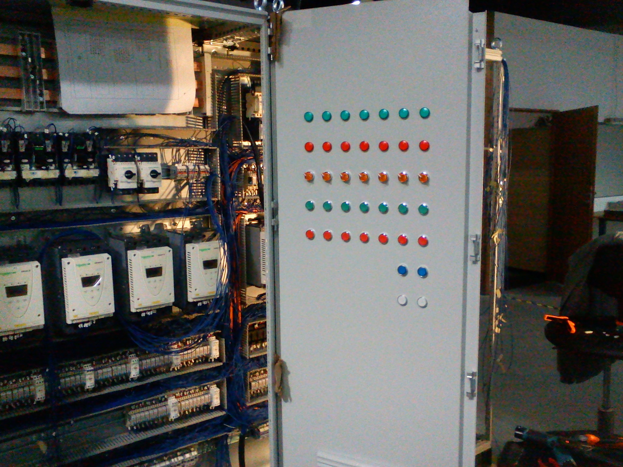 Otwarta szafa sterownicza z widocznymi elementami elektrycznymi, w tym liczniki energii, przekaźniki i okablowanie; na drzwiach szafy rząd diod sygnalizacyjnych w kolorach zielonym, czerwonym...