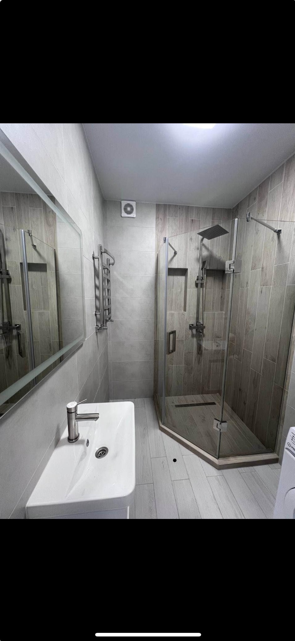 Nowoczesna łazienka z kabiną prysznicową typu walk-in, umywalką nablatową i grzejnikiem drabinkowym w odcieniach szarości i beżu, wykończona płytkami imitującymi drewno.